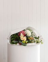 The Wild flower Pastel bouquet featuring pink, white, and nude blooms wrapped in white paper on a white pedestal.
