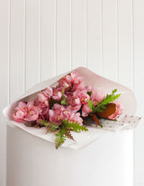 The Wild flower Cymbidium Orchid Stem bouquet in pink, wrapped in white paper with seasonal foliage.