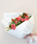The Wild flower Seasons Best bouquet featuring pink ruffled tulips and seasonal greenery wrapped in white paper.