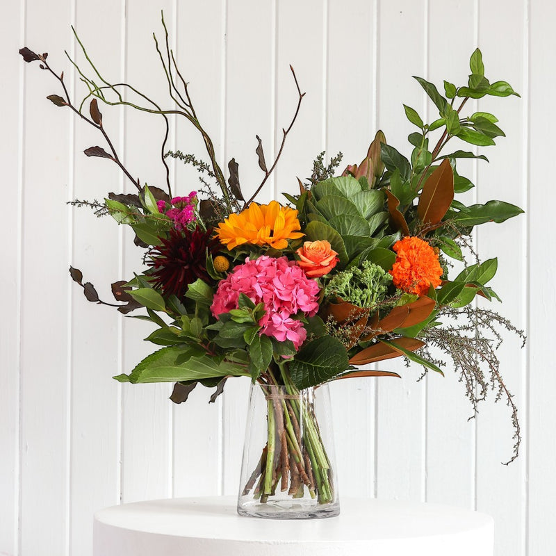 The Wild flower Florist Surprise bouquet featuring bright seasonal flowers like pink hydrangea and orange dahlias in a vase