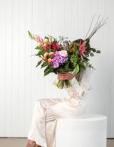 The Wild flower Florist Surprise bouquet featuring vibrant seasonal pink, purple, and peach blooms held by a model.