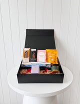 The Wild flower gourmet artisan gift hamper featuring assorted snacks, sweets, and a candle in a black gift box.