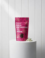 The Wild flower little bird organics Cacao Raspberry Good Macaroons snack pack in a pink pouch on a white pedestal.