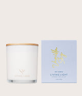 The Wild flower Living Light scented candle in a glass jar with a wooden lid next to its light blue packaging box.