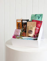 The Wild flower Luxury Treat Box featuring gourmet snacks, cookies, and a soy candle in a white gift box with flowers.