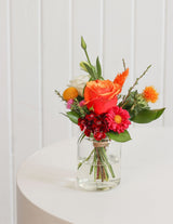 The Wild flower Petite arrangement featuring vibrant orange, pink, and white flowers in a small glass jar.