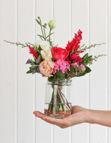 The Wild flower Petite arrangement featuring a mix of vibrant pink, red, and white flowers in a small glass jar.