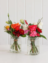 The Wild flower Petite floral arrangements featuring vibrant roses and mixed blooms in small glass jars on a table.