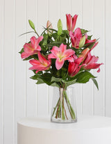 The Wild flower Lily Bouquet featuring vibrant pink oriental lilies and lush green foliage in a clear glass vase.