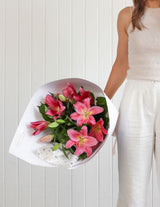 The Wild flower Lily Bouquet featuring vibrant pink oriental lilies and green foliage wrapped in elegant white paper.