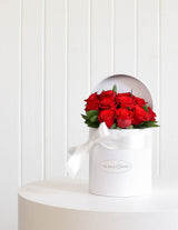The Wild flower Juliet arrangement featuring a dozen red roses in a white hatbox with a white ribbon on a table.