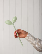 The Wild flower sage green leaf-shaped soil moisture indicator tool held in a hand for indoor plant care.