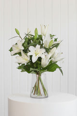 The Wild flower Lily Bouquet featuring fresh white oriental lilies and green foliage in a clear glass vase